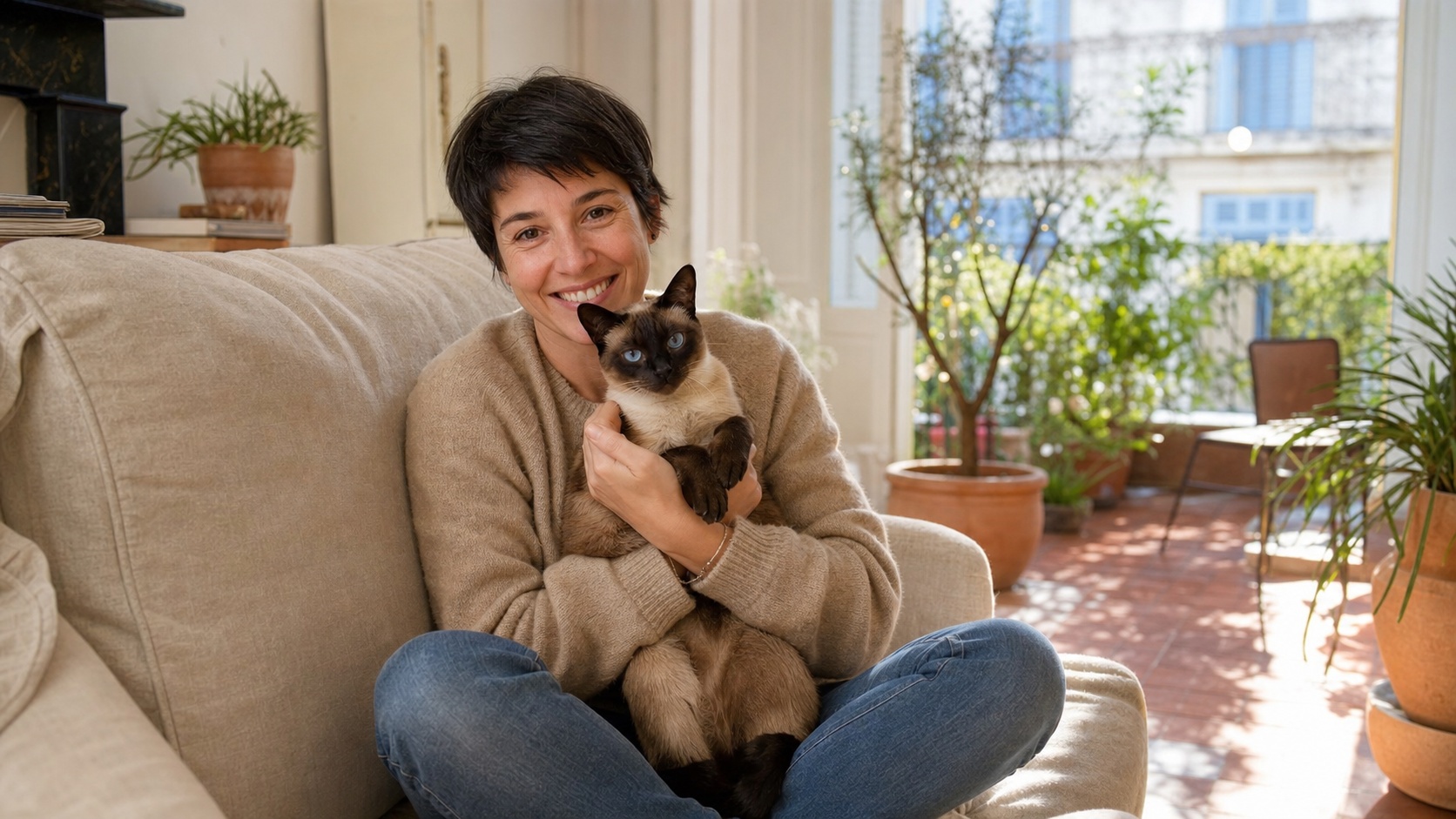 Propriétaire sereine tenant son chat siamois dans les bras à la maison, environnement chaleureux et lumineux