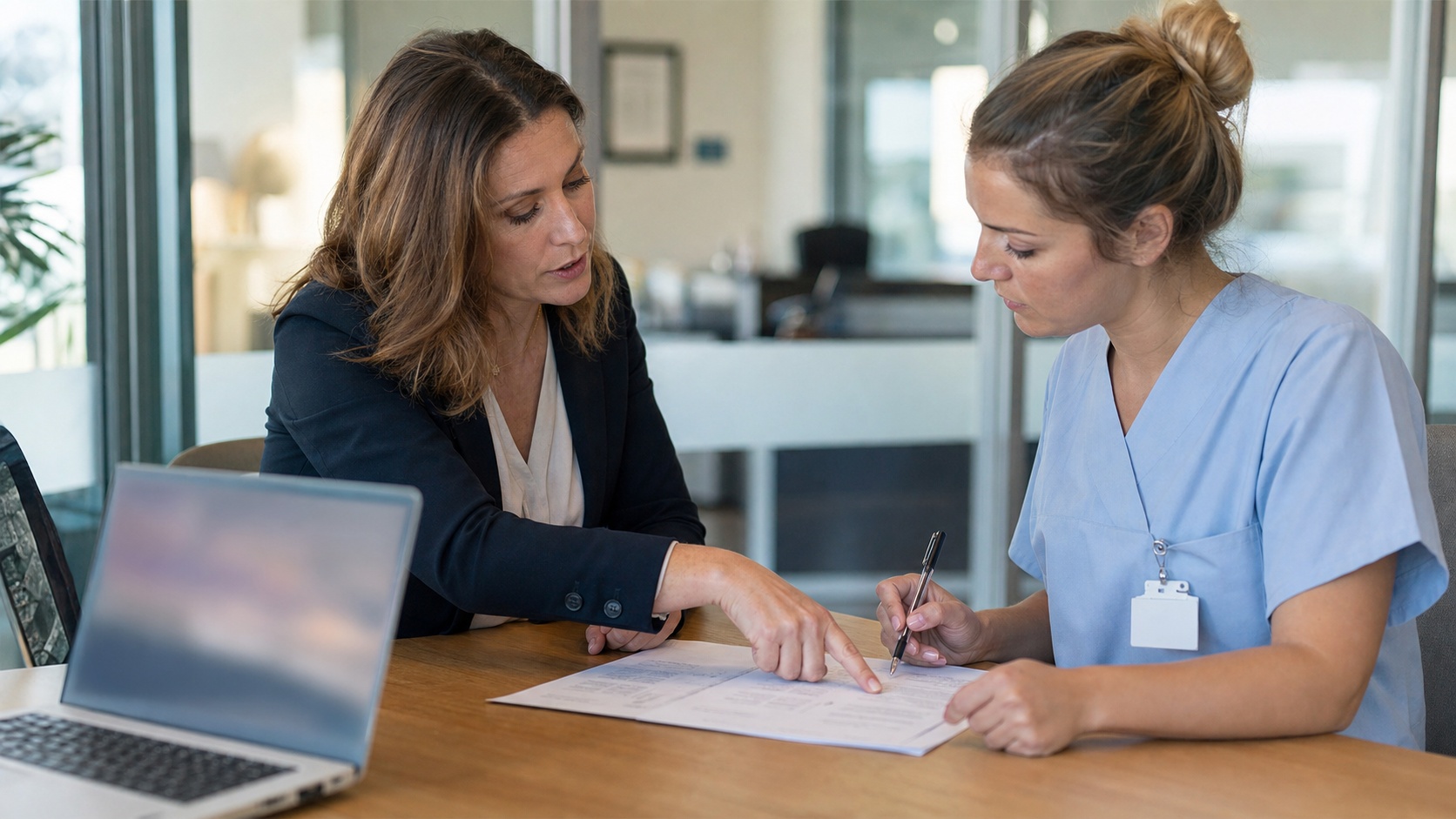 Sage-femme et conseiller en assurance comparant des formules de prévoyance TNS sur un écran dans un bureau